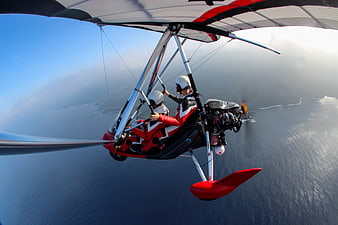 Two people flying a red ultralight aircraft over the ocean