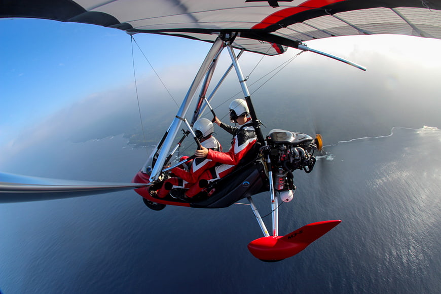 Two people flying a red ultralight aircraft over the ocean