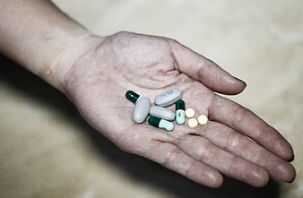 Hand holding various pills and capsules for medication