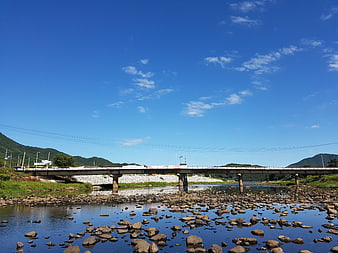 Concrete bridge over rocky river with blue sky and mountains