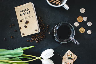 Flat lay of coffee, field notes, coins, and white tulips