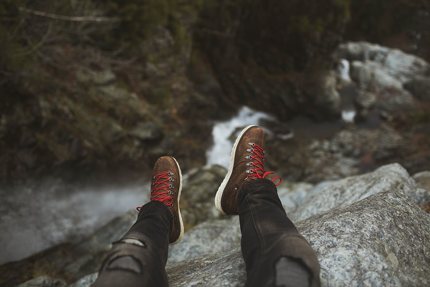 First-person view of hiking boots dangling over a rocky stream