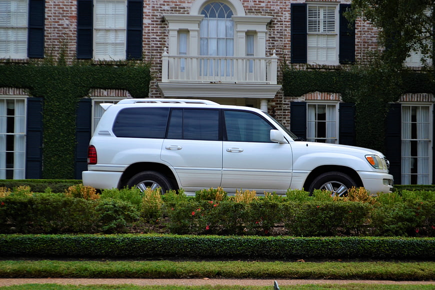 White SUV parked in front of luxury brick mansion with hedges