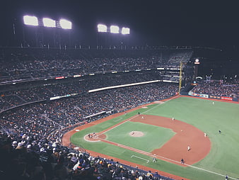 Night baseball game in crowded stadium with bright floodlights