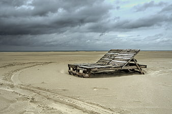 Weathered wooden pallet bed on empty sandy beach under stormy sky