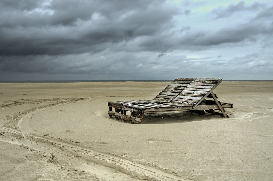 Weathered wooden pallet bed on empty sandy beach under stormy sky
