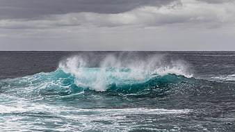 Powerful turquoise ocean wave crashing under cloudy sky