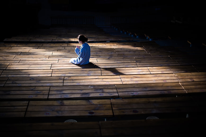 Woman sitting alone on wooden stage in spotlight