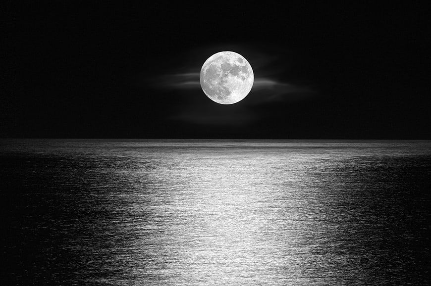 Full moon over calm ocean at night in black and white
