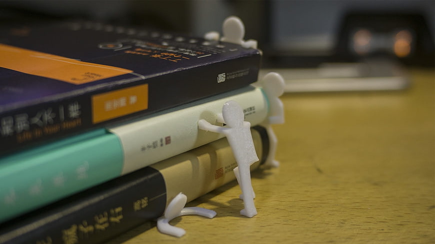 Miniature figures pushing a stack of books on a desk