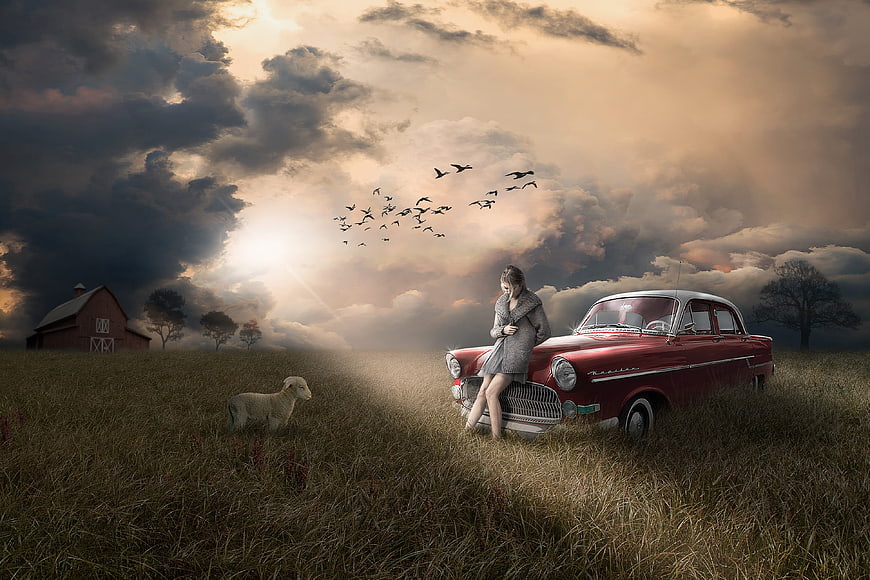 Woman leaning on vintage red car in dramatic field