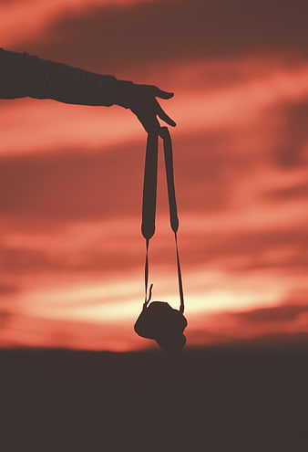 Silhouette of Hand Holding Camera Against Red Sunset Sky