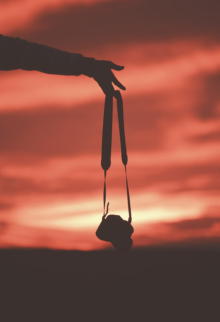 Silhouette of Hand Holding Camera Against Red Sunset Sky