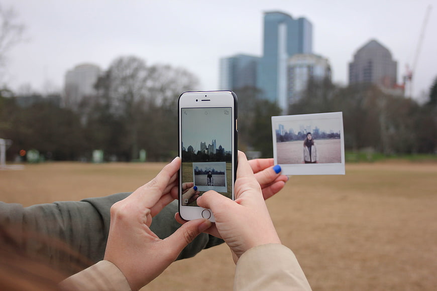 Hands holding smartphone and polaroid photo in city park