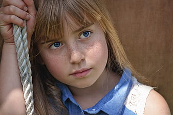 Close-up portrait of a freckled girl with blue eyes holding a rope