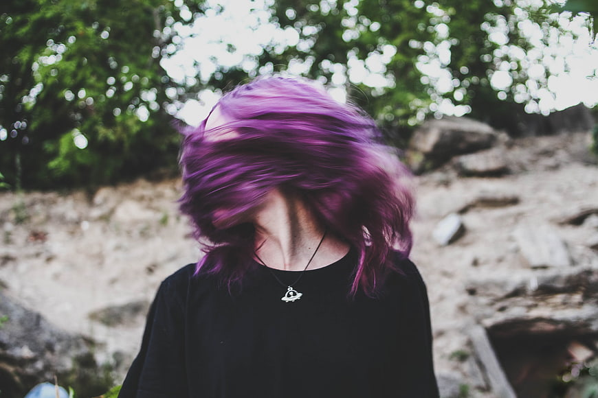 Woman with vibrant purple hair shaking head outdoors