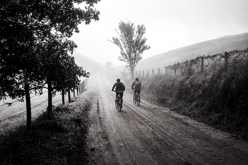 Two Cyclists Riding on Foggy Dirt Road in Black and White