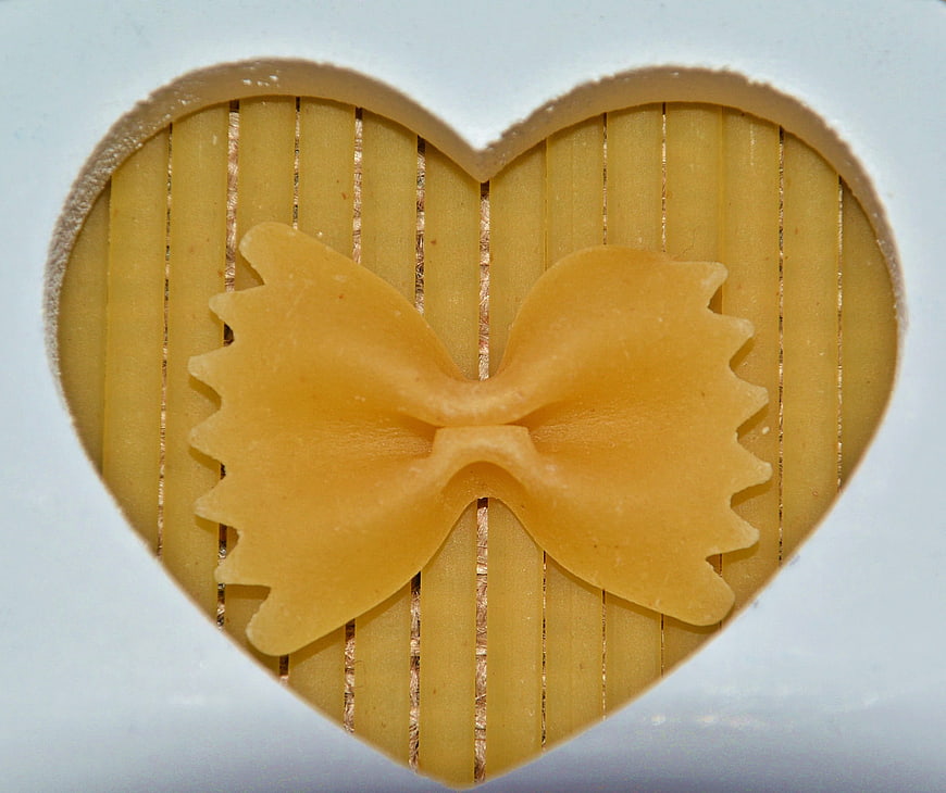 Farfalle pasta in heart-shaped frame with spaghetti background