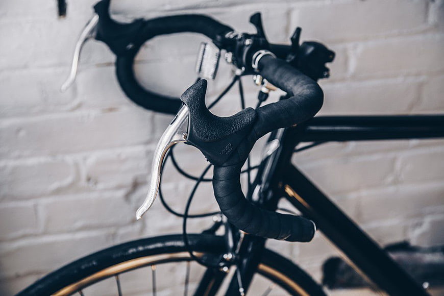 Close-up of black road bike handlebars against white brick wall