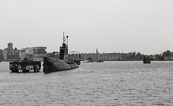 Black submarine docked in Amsterdam harbor with city skyline
