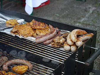 Assorted grilled sausages and meat cooking on charcoal barbecue