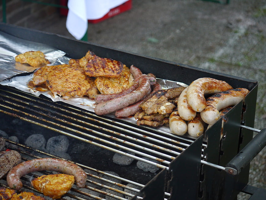 Assorted grilled sausages and meat cooking on charcoal barbecue