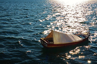 Traditional wooden boat with sail on sparkling blue sea