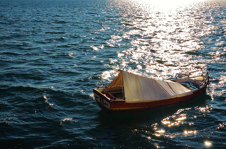 Traditional wooden boat with sail on sparkling blue sea