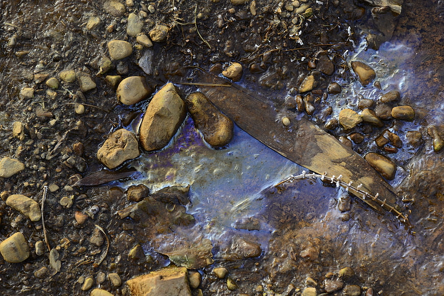 Oil slick pollution in stream with rocks and debris