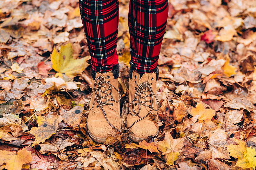 Woman's legs in plaid pants and boots on autumn leaves