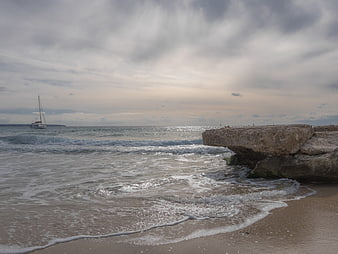 Sailboat on Ocean with Rocky Outcrop and Cloudy Sky