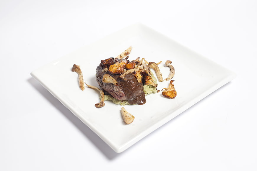 Gourmet steak dish with mushrooms on white square plate