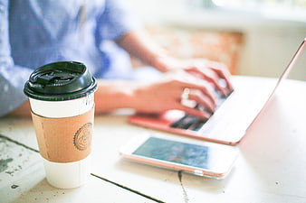 Coffee cup on desk with person typing on laptop