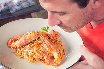 Man smelling shrimp pasta dish in red shirt