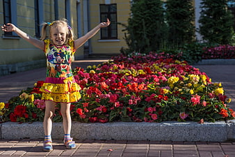 Happy little girl with arms raised standing by colorful flower bed