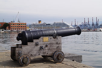 Historic cannon on harbor pier with cruise ship background