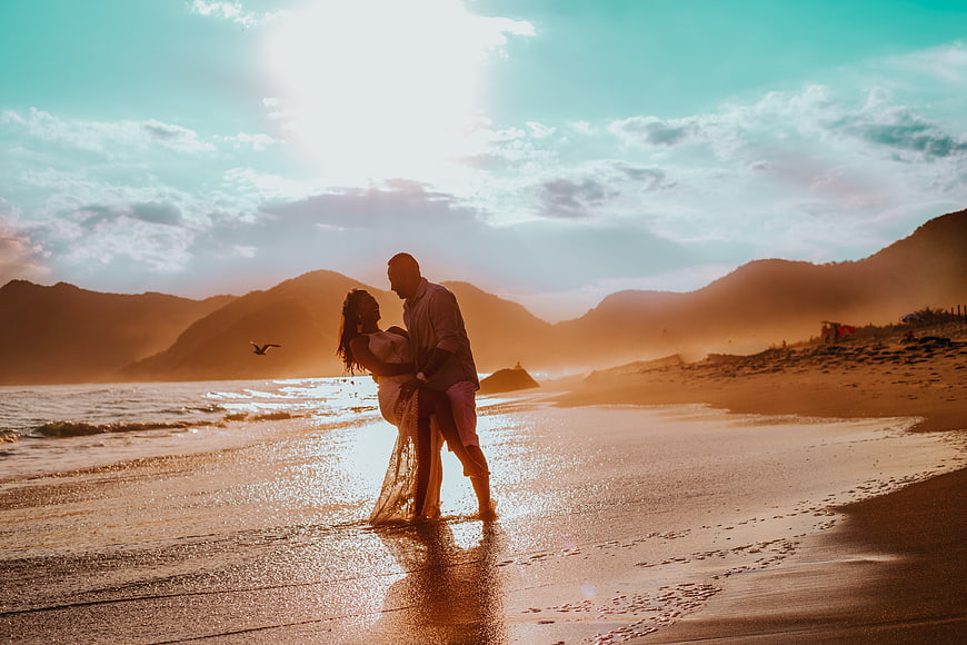 Romantic couple embracing on beach at sunset with mountains
