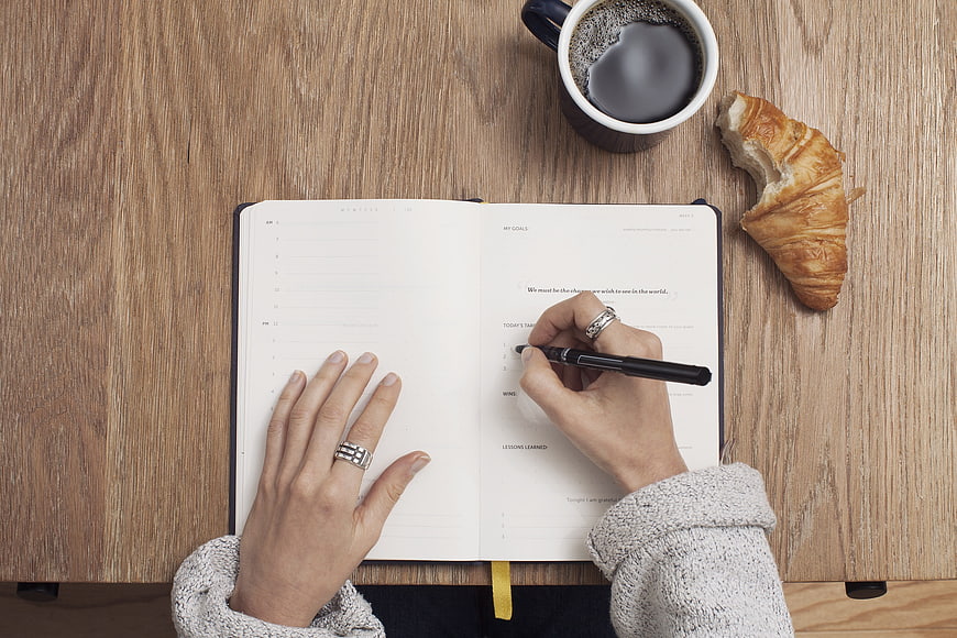 Top view of hands writing in planner with coffee and croissant