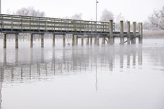 Foggy wooden pier over calm lake in winter morning