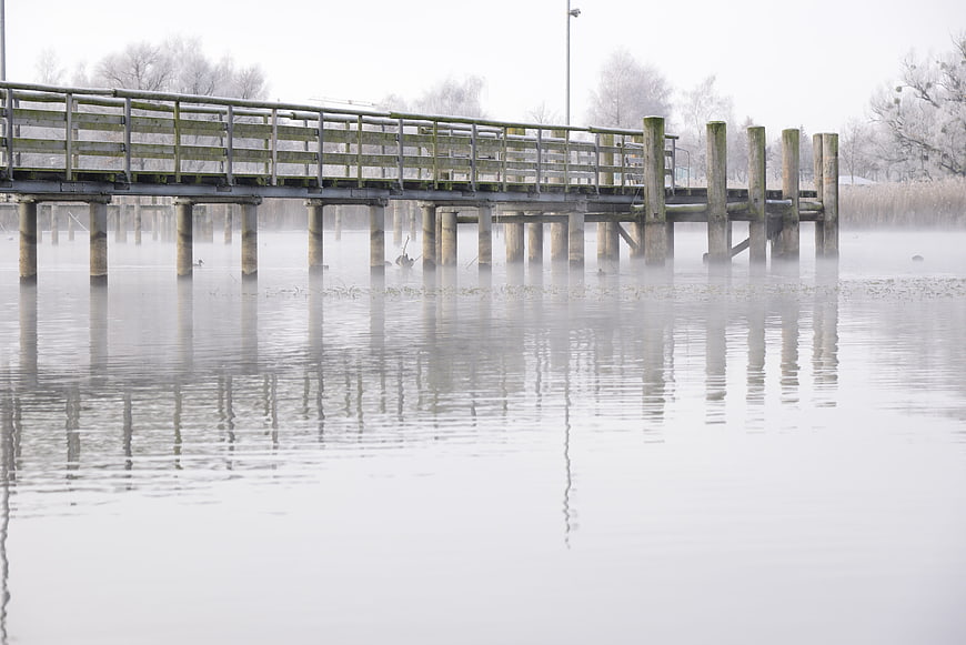 Foggy wooden pier over calm lake in winter morning