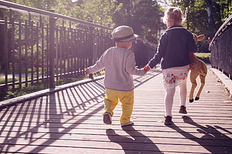 Two children holding hands walking on a wooden bridge