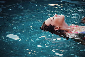 Relaxed woman floating in blue swimming pool water