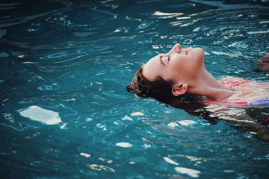 Relaxed woman floating in blue swimming pool water