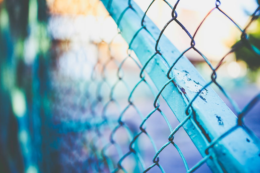 Close-up of weathered blue chain-link fence with blurred background