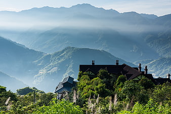 Mountain lodge nestled in lush green hills with misty peaks