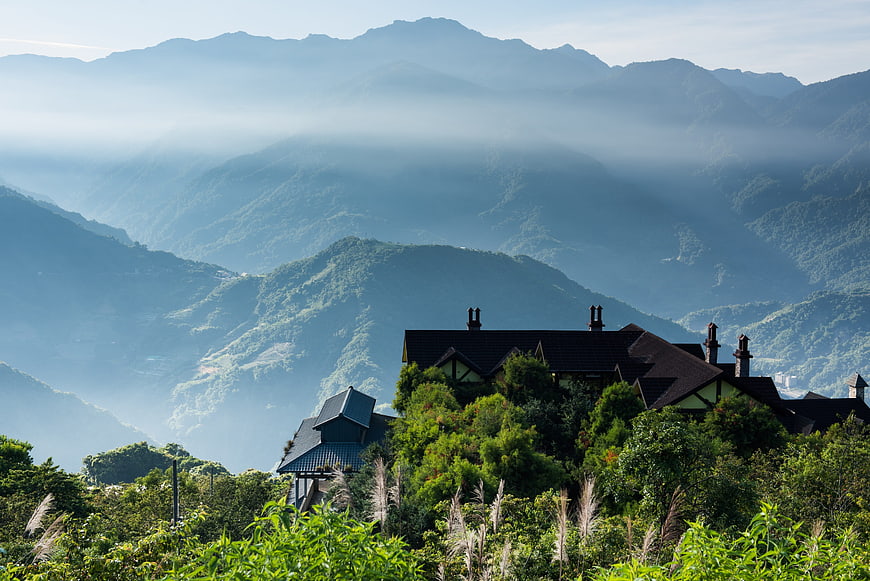 Mountain lodge nestled in lush green hills with misty peaks