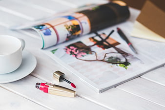 Lip gloss, coffee cup, and magazine on white wooden table