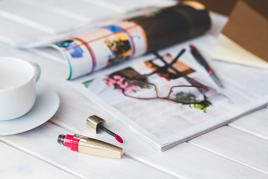 Lip gloss, coffee cup, and magazine on white wooden table