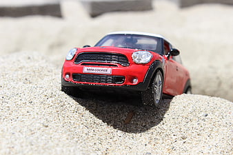 Red Mini Cooper toy car stuck in sand