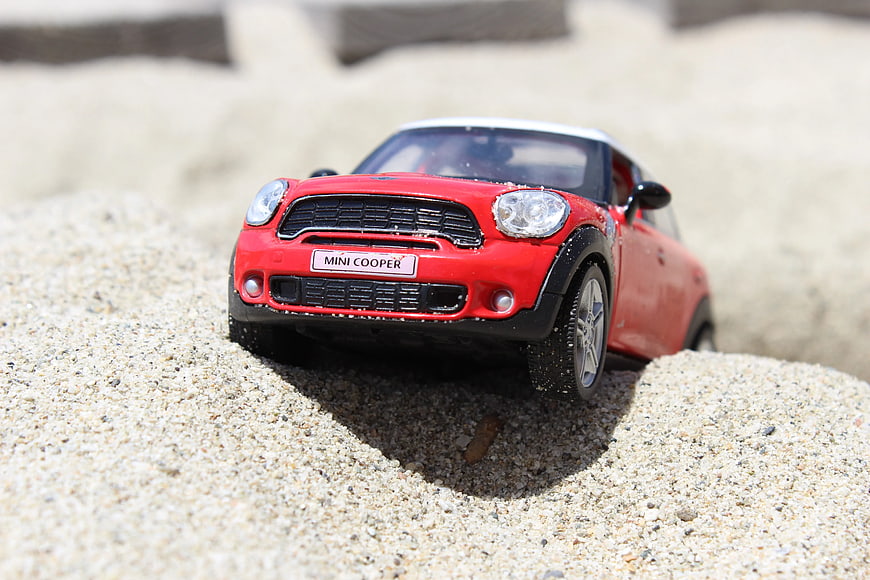 Red Mini Cooper toy car stuck in sand